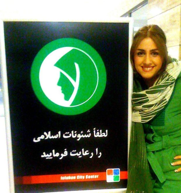 δίπλα σε μια πινακίδα που υπενθυμίζει στις γυναίκες να  συμμορφώνονται με τους κανόνες του ισλάμ